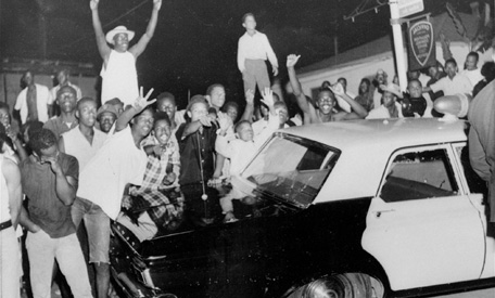 Demonstrators push against a police car after rioting erupted in a crowd of 1,500 in the Los Angeles area of Watts.  14,000 national guardsmen were called in to disperse the rioting and over 100 square blocks were destroyed by arson.